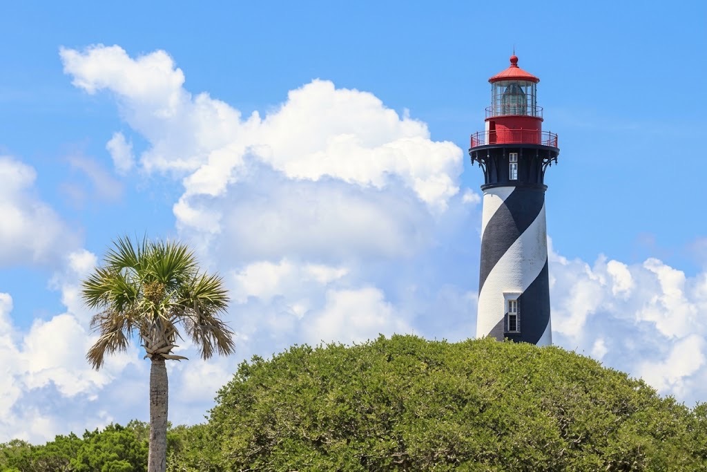 St. Augustine Lighthouse in Florida, with its black-and-white spiral tower, red lantern, and a palm tree